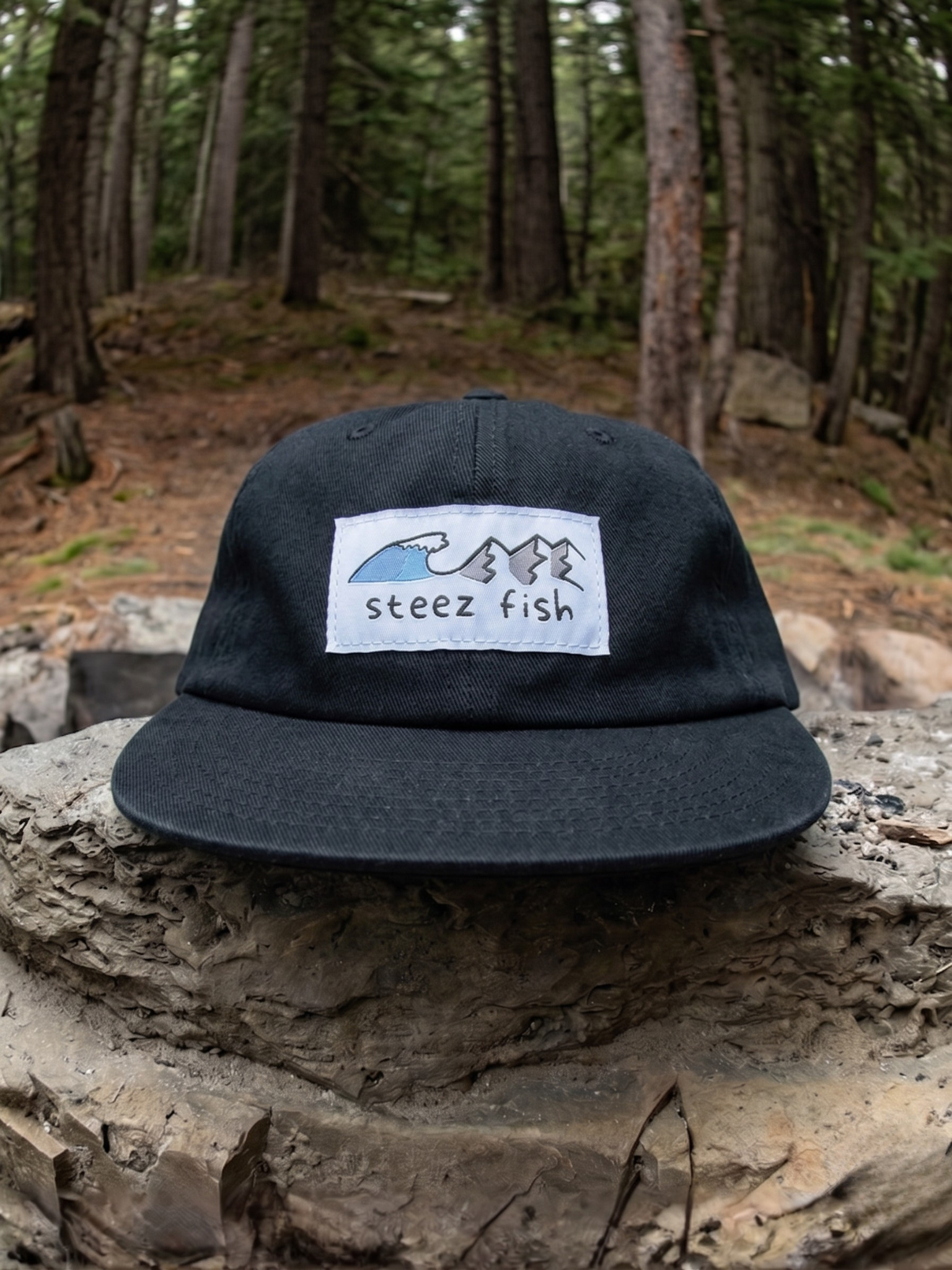 Black cap with a logo and text 'steez fish' on a rock in a forest setting