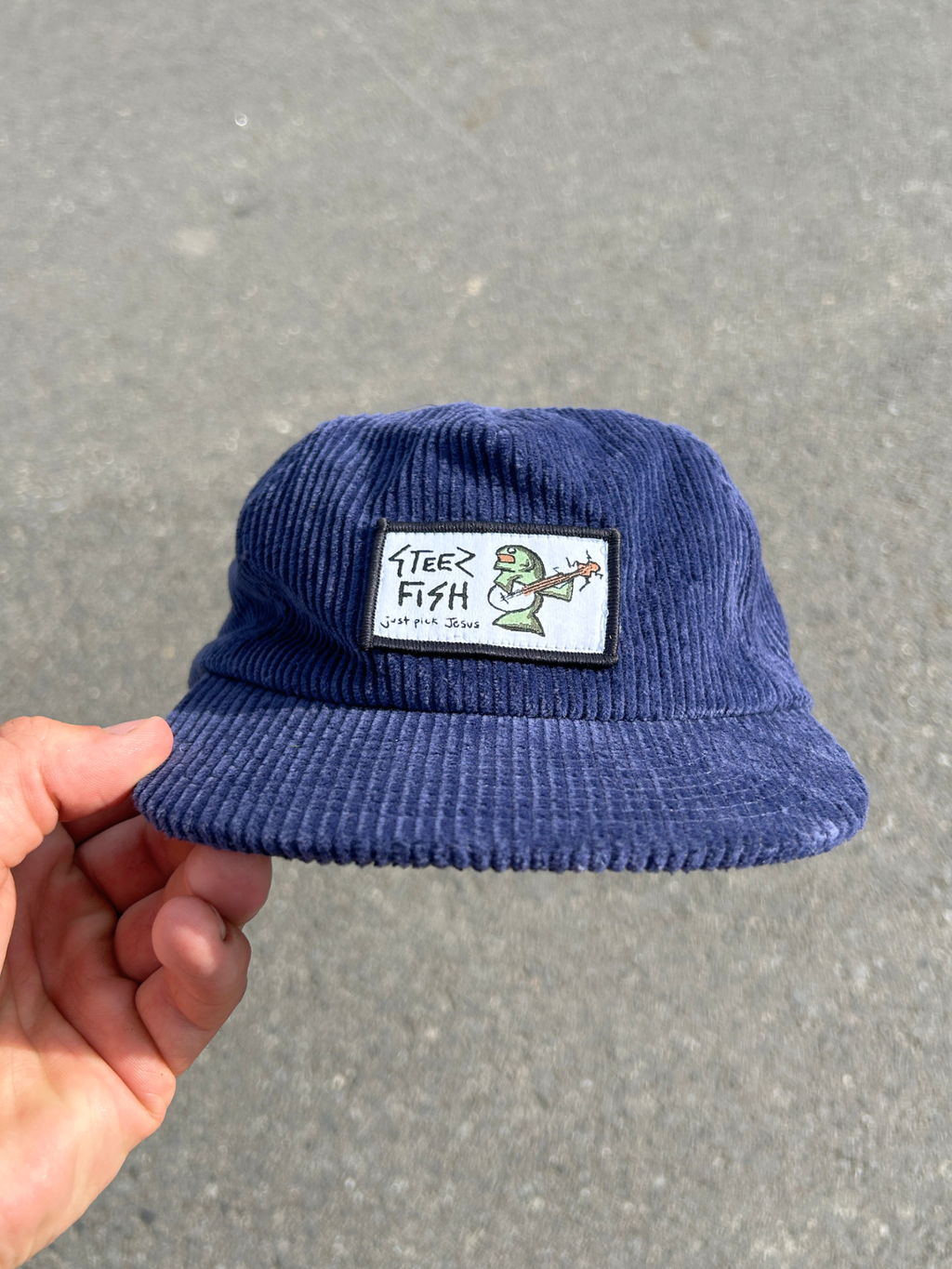 Blue corduroy hat with a patch held by a hand on a gray background