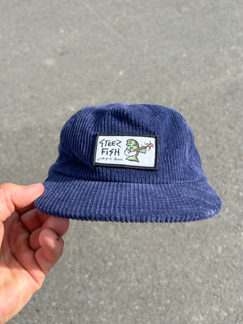 Blue corduroy hat with a patch held by a hand on a gray background