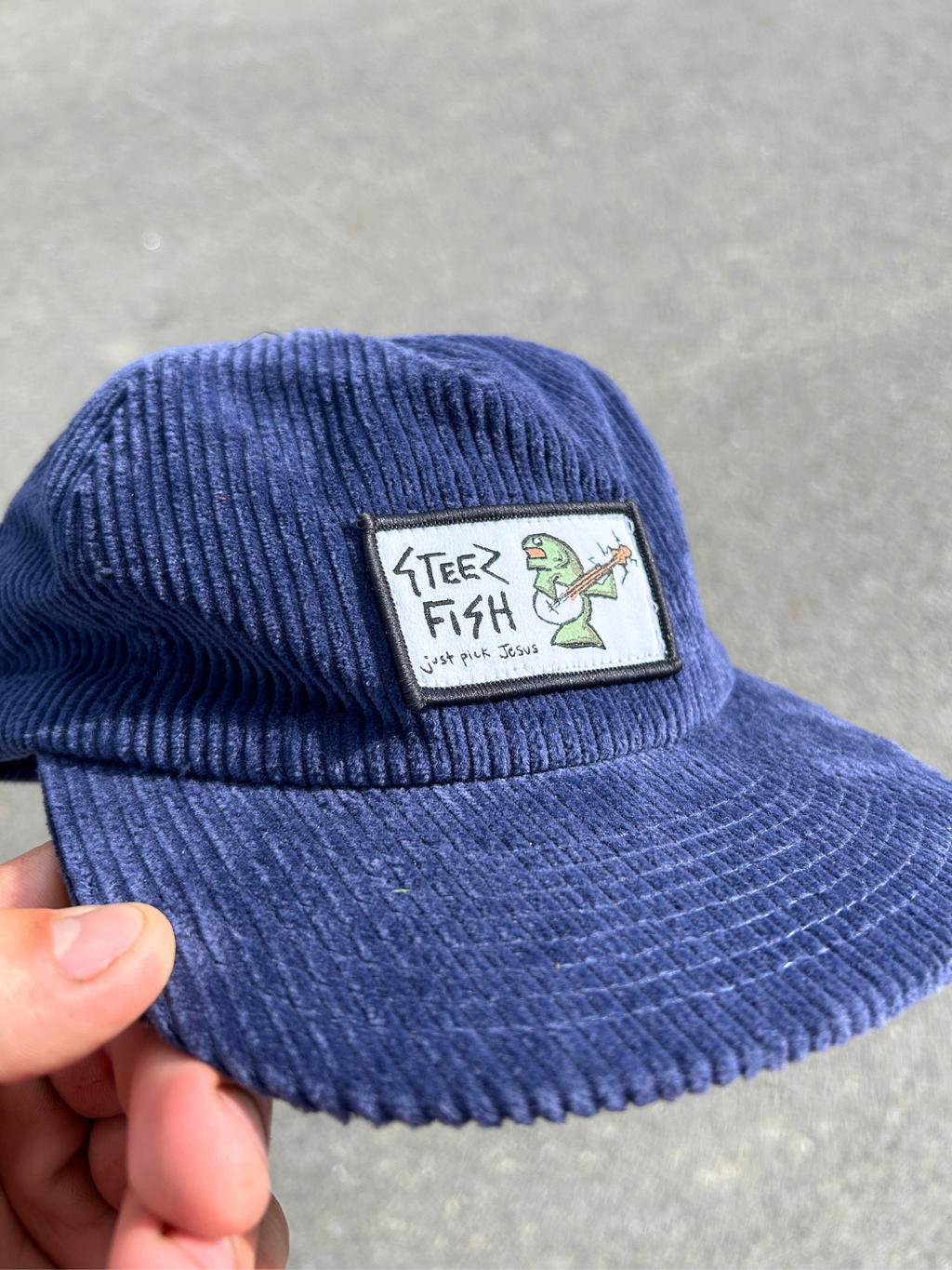 Blue corduroy cap with a patch featuring a cartoon character on a gray background