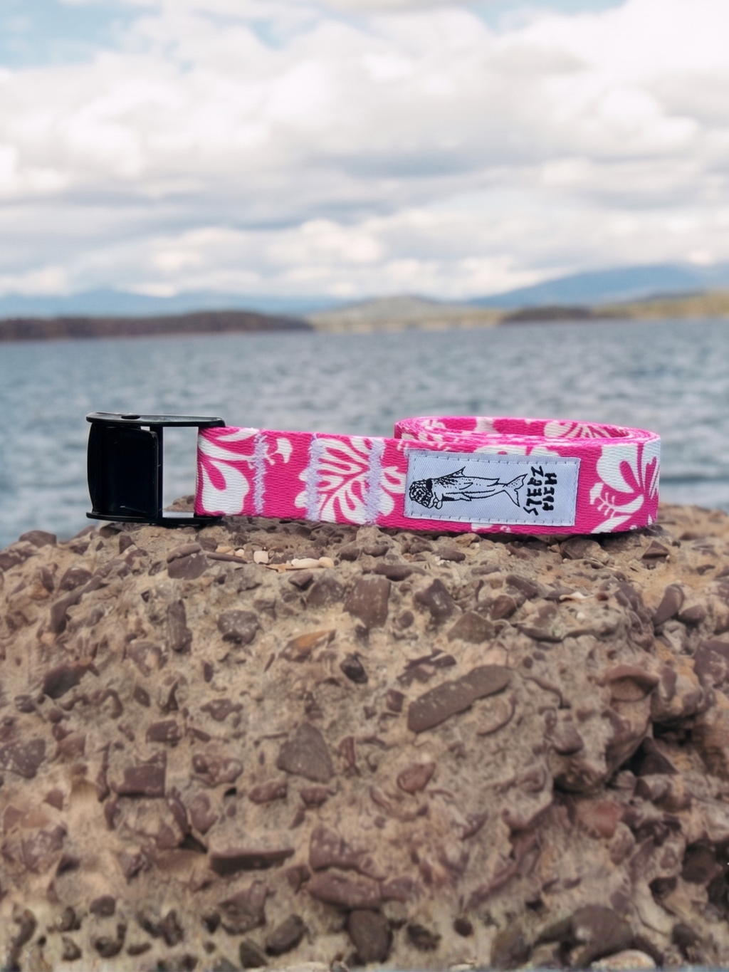 Pink and white patterned belt with black buckle on a rock by a lake