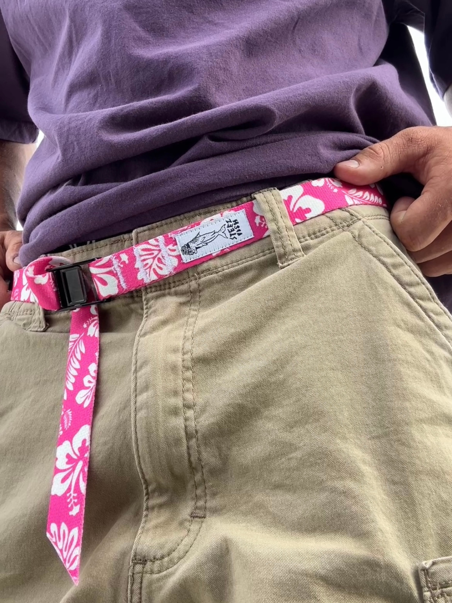 Person wearing a pink belt with a floral pattern on beige pants.